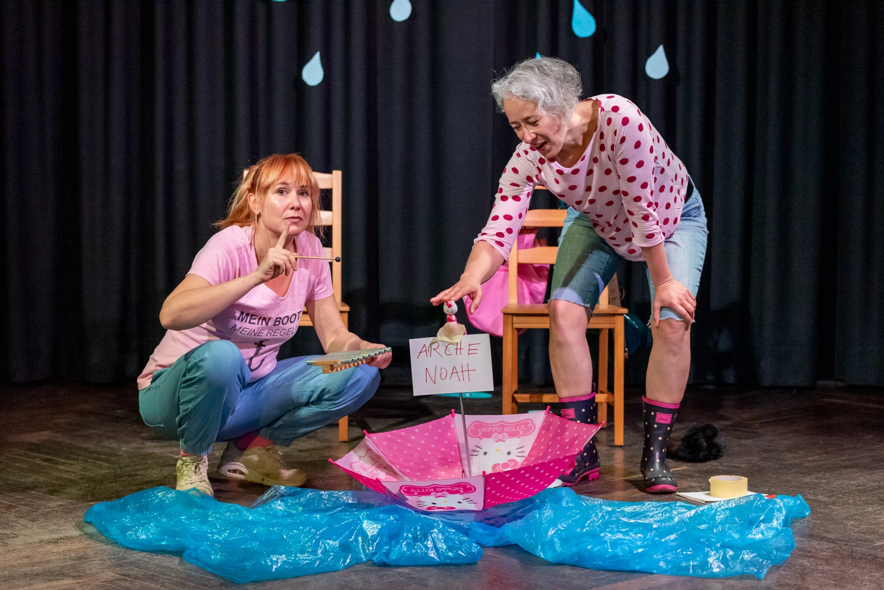 Jana and Jule performing ARCHA with an umbrella boat and blue rain scenery
